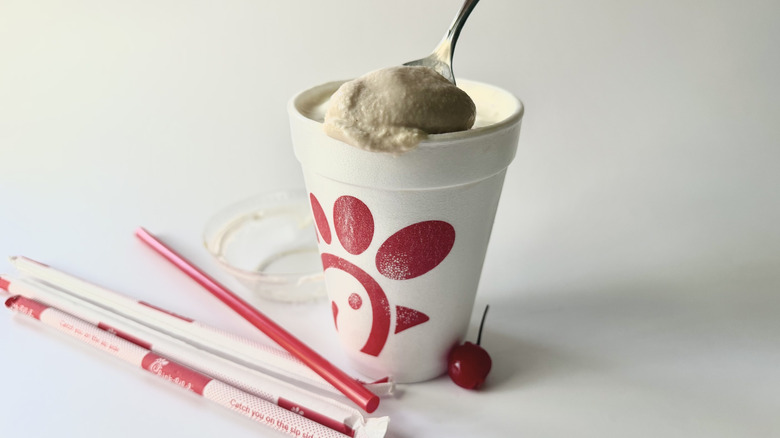Chick-fil-A's Chocolate Milkshake with a spoon inserted into the cup next to a cherry, straws, and the lid
