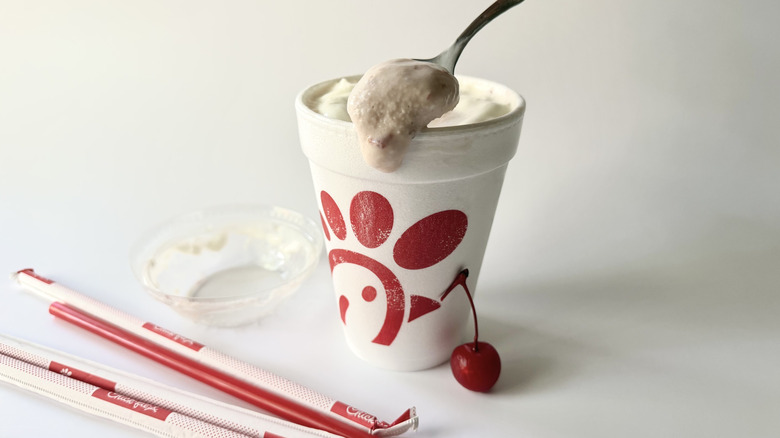 Chick-fil-A's Strawberry Milkshake with a spoon inserted into the cup next to a cherry, straws, and the lid