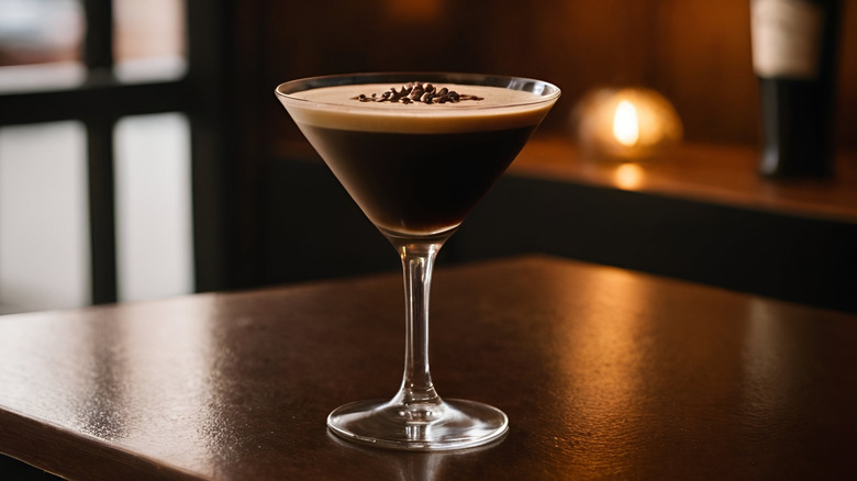 A single espresso martini sits on a wooden table surrounded by spilled coffee beans, against a black background