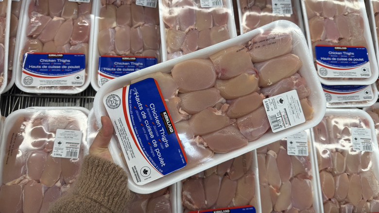 Hand holding a package of Kirkland Signature Fresh Boneless Skinless Chicken Thighs