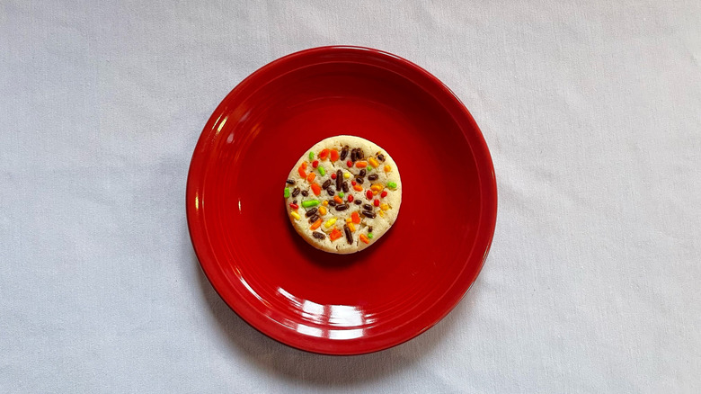 A sugar cookie topped with brown, red, orange, and green sprinkles on a red plate