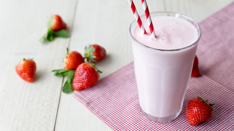 A glass of strawberry milk surrounded by strawberries