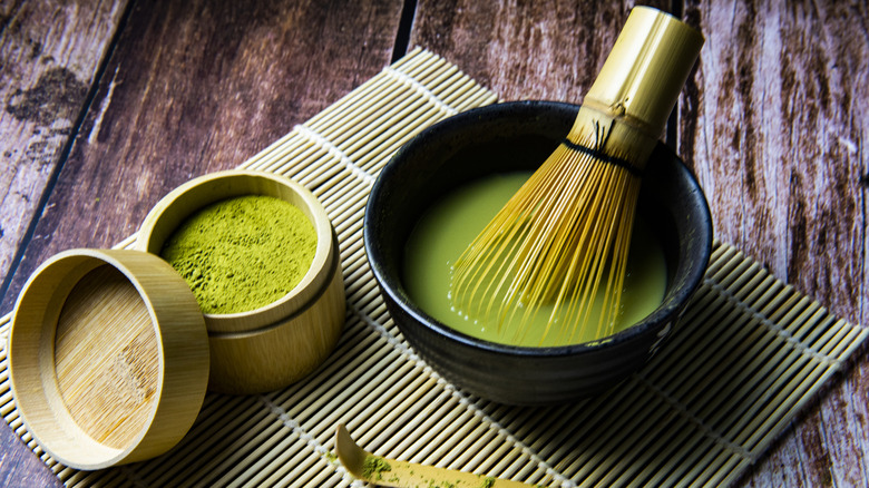 Powdered matcha next to a bowl of whisked matcha and a whisk