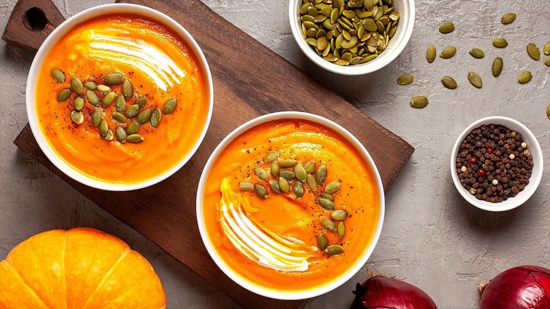 Bowls of pumpkin soup with pumpkin seeds on a wood serving board