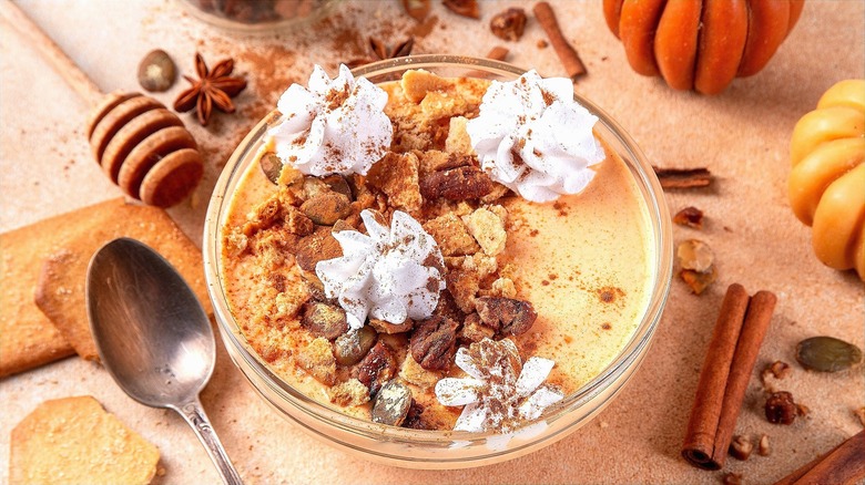 Bowl of Greek yogurt mixed with pumpkin puree and topped with pumpkin seeds, pecans, cinnamon, and dollops of whipped cream