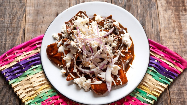 Mole chilaquiles topped with crumbled queso fresco and sliced red onion on a white plate