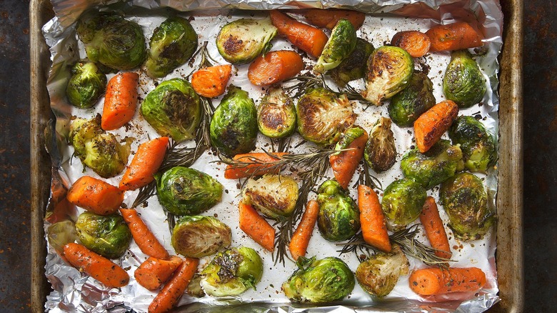 Roasted halved Brussels sprouts and chopped carrots on a foil-lined sheet pan