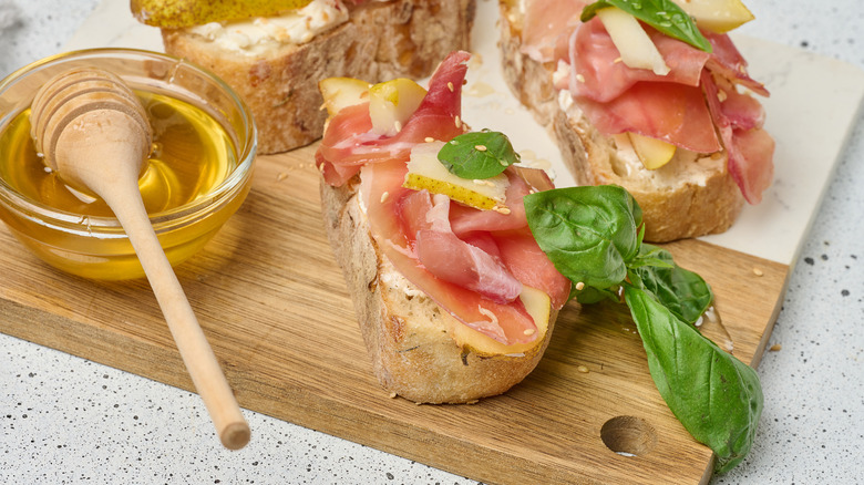 Honey on bread with meat and pear slices on a wooden board