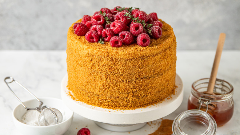 Honey cake with raspberries on top and bowls of honey and powdered sugar on the side