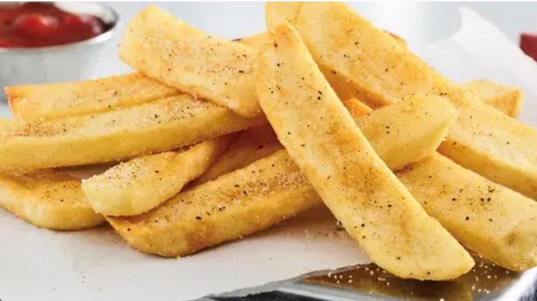 A pile of steak fries with seasoning and a small container of ketchup in the background