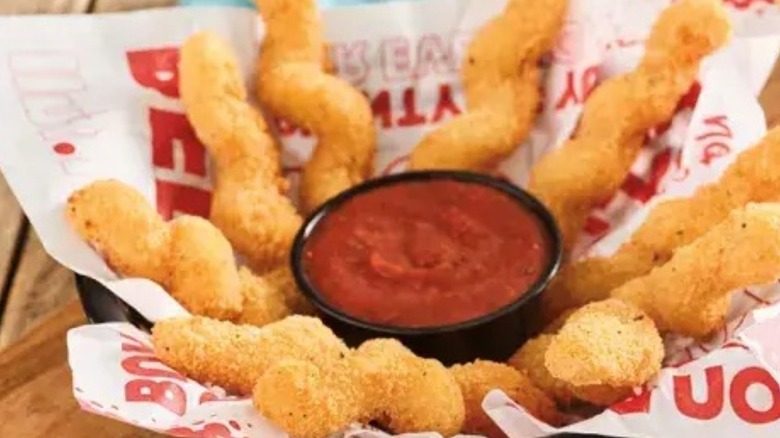 Breaded, twisted mozzarella sticks surrounding a container of sauce, all on a paper wrapper