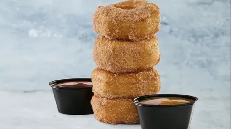 A short stack of cinnamon doughnuts with two containers of chocolate and caramel sauces on either side