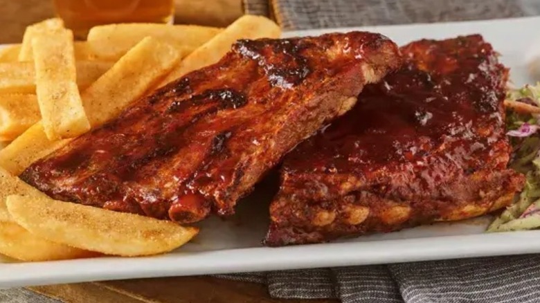 Two slabs of Whiskey River BBQ ribs on a white plate next to steak fries and coleslaw