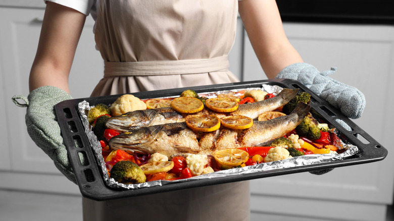 Person holding tray with cooked, lemon-topped whole sea bass and vegetables