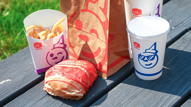 Jack in the Box burger, fries, drinks, and bag on a picnic table