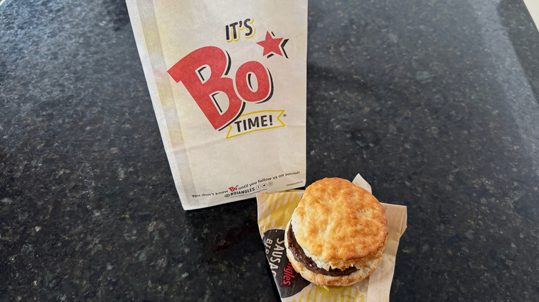 Bojangles sausage biscuit on its wrapper with takeout bag behind it