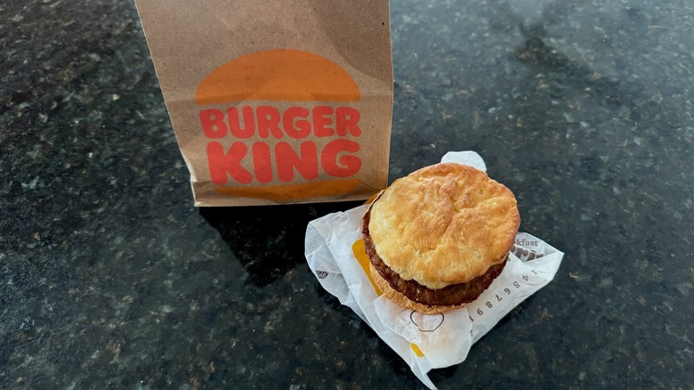 Burger King sausage biscuit on its wrapper with takeout bag behind it