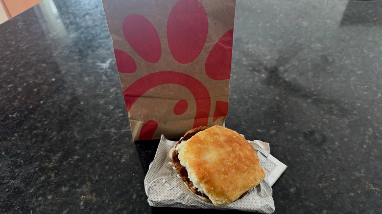 Chick-fil-A sausage biscuit on its wrapper with takeout bag behind it