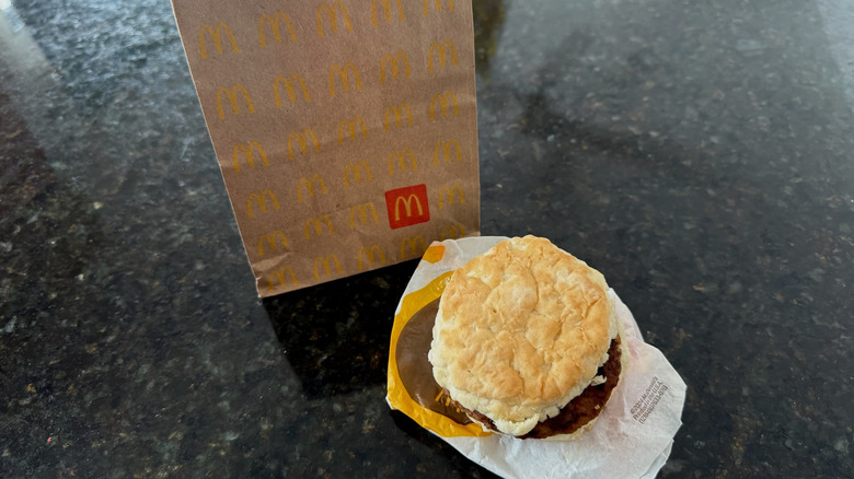McDonald's sausage biscuit on its wrapper with takeout bag behind it