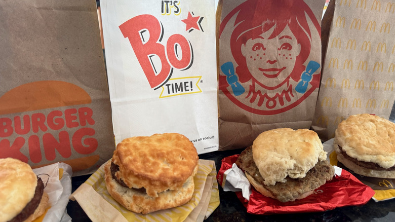 lineup of fast food sausage biscuits with takeout bags behind them