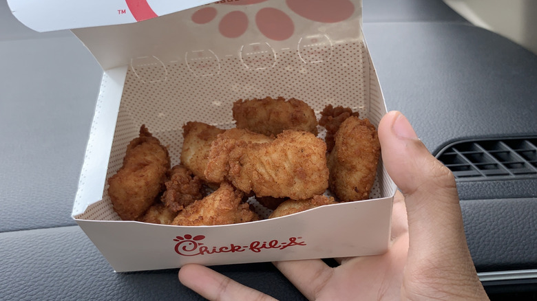 Close-up of a hand holding a box of Chick-fil-A chicken nuggets against a car dashboard