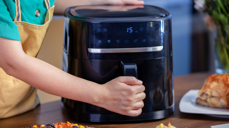 Person pulling open a black air fryer sitting on a counter top.