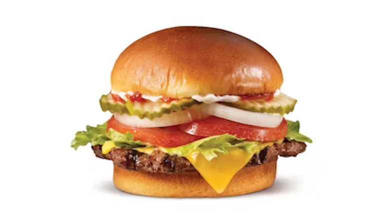 A Hardee's burger loaded with lettuce, tomatoes, pickles, and cheese on a white background