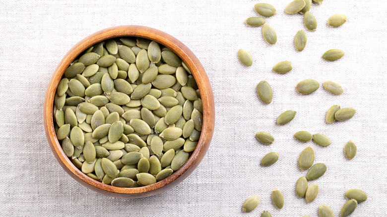 Pumpkin seeds, or pepitas, in a wooden bowl and scattered on fabric