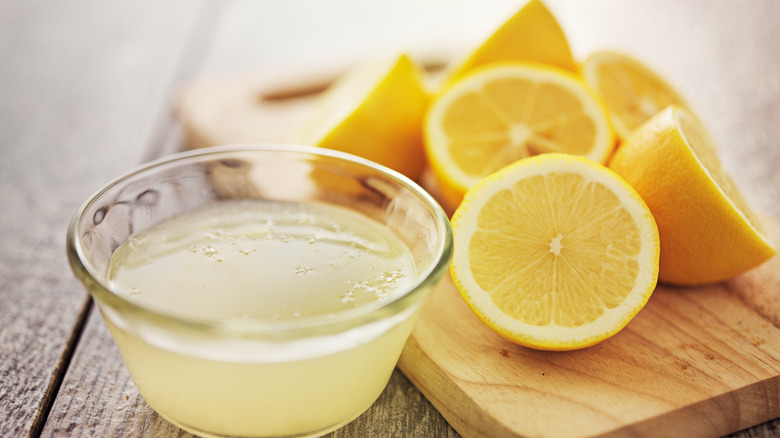 Cut lemons on a cutting board with a bowl of squeezed lemon juice