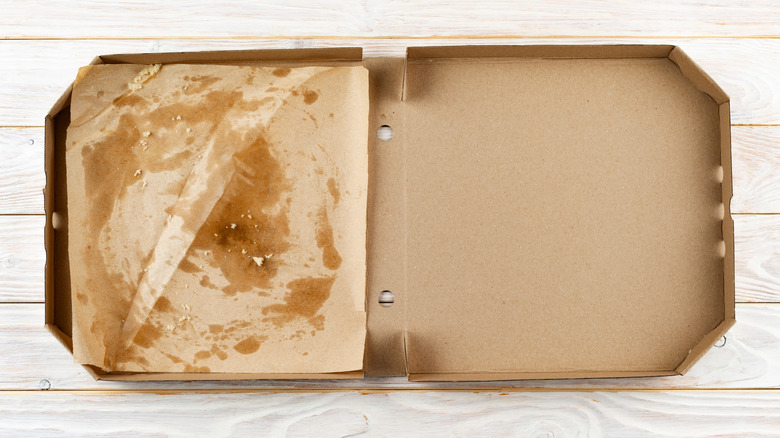 Greasy pizza box on top of light wood colored table.