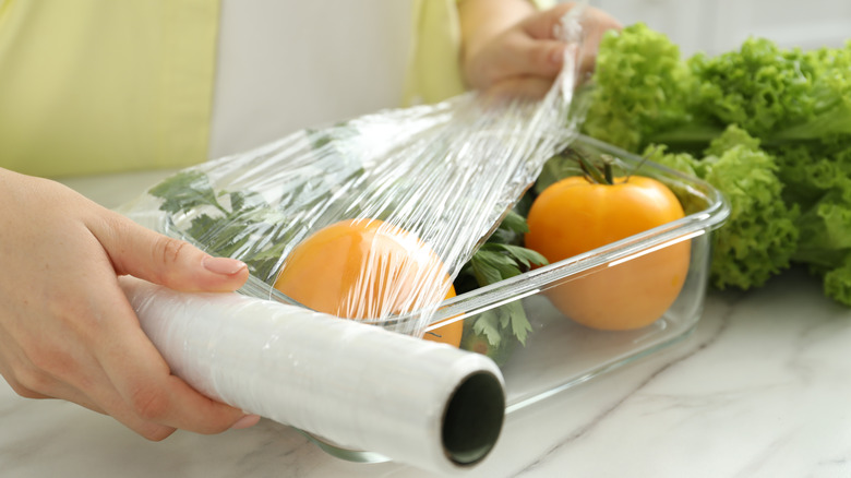 Woman using plastic film to cover glass container of produce.