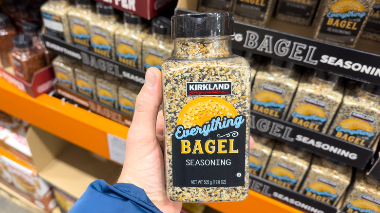 Person holding a container of Kirkland Signature Everything Bagel Seasoning in front of store shelf