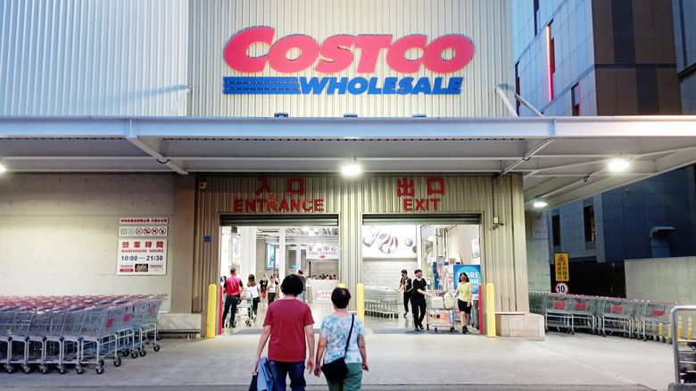 Two shoppers entering Costco wholesale warehouse near front entrance and grocery carts