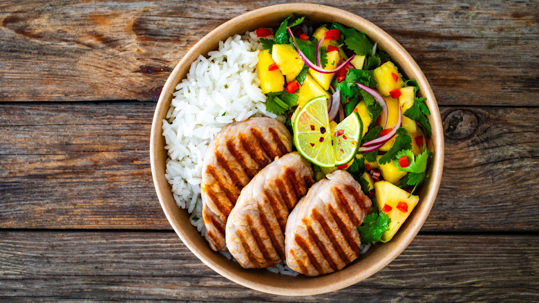 Pork and rice in a bowl with greens on a wooden table