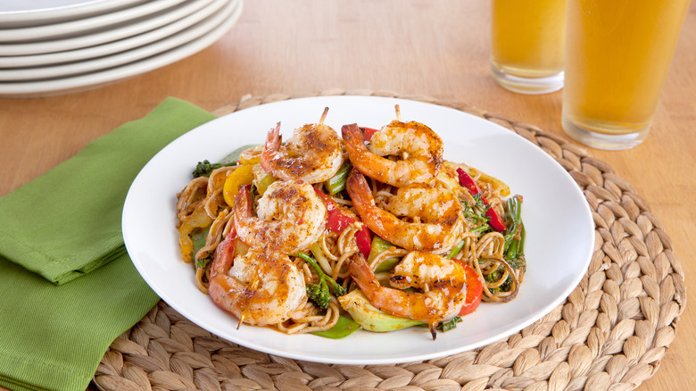 Shrimp on noodles and greens on a placemat on a table