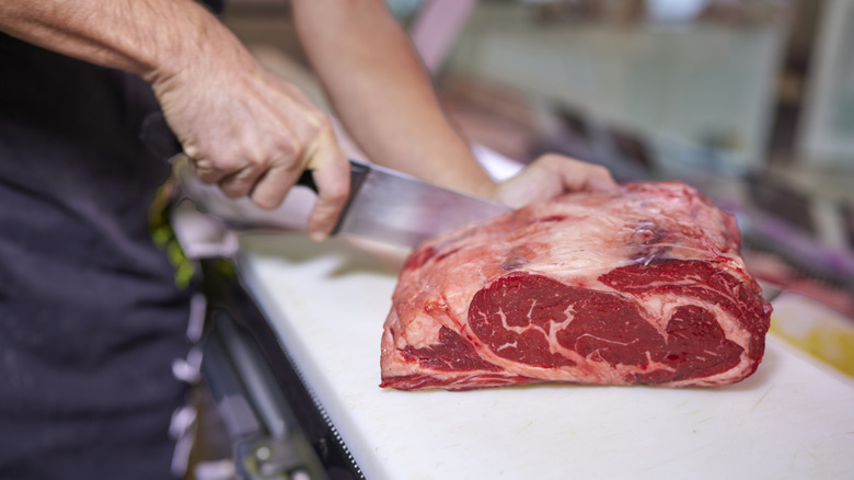 Person cutting raw meat on a cutting board in a restaurant kitchen