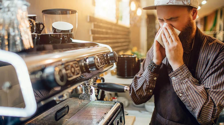 Barista blowing his nose behind coffee service counter