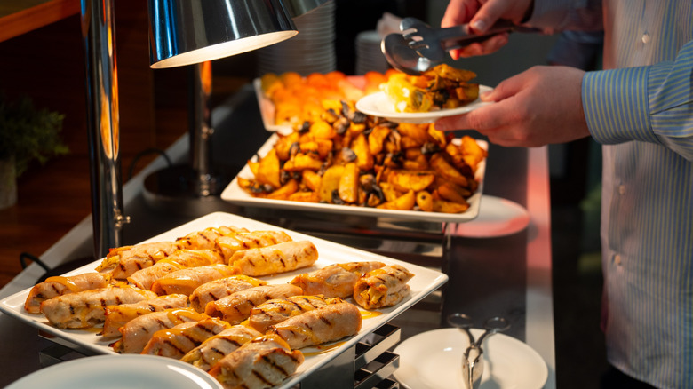 Person taking food from serving plates under heat lamps at a buffet