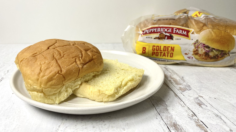 A Pepperidge Farm Golden Potato Hamburger Bun on a white plate in front of its packaging on a white surface,