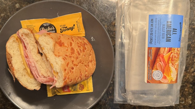 Sub sandwich on gray plate beside packaging