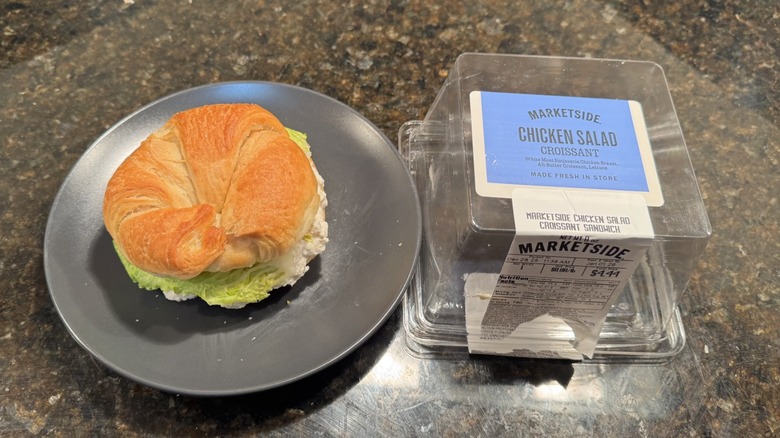 Chicken salad croissant on a gray plate beside packaging