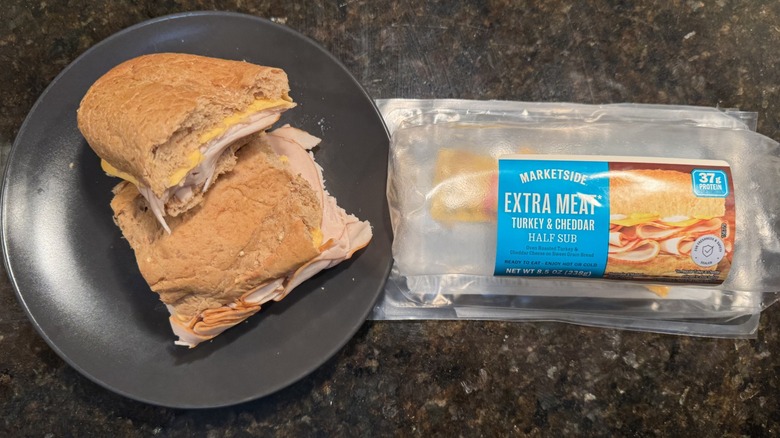 Extra meat and turkey sandwich on gray plate beside packaging