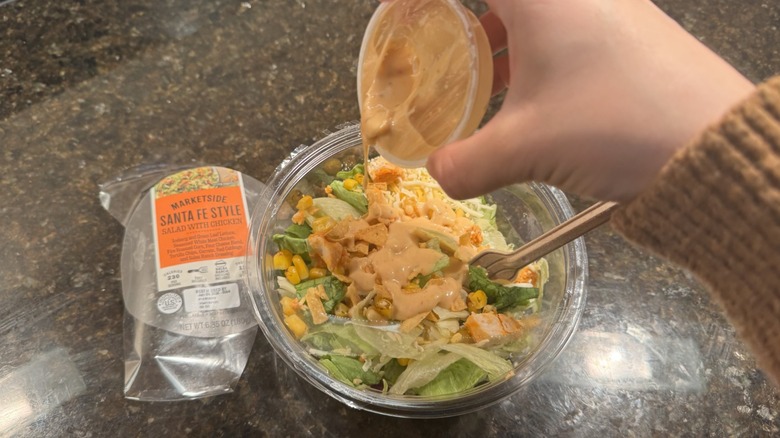 Hand pouring dressing on a Santa Fe salad