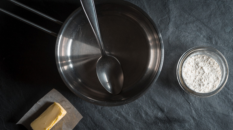 A frying pan with a spoon in it alongside a bowl of flour and a stick of butter