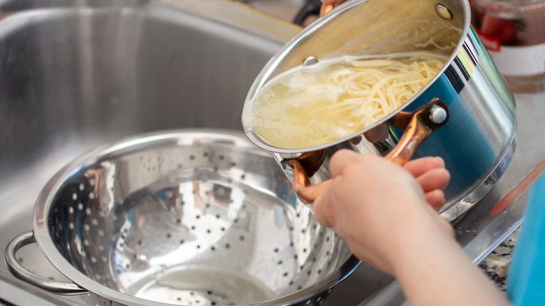 A cook preparing to drain a pot of pasta in a colander over a sink