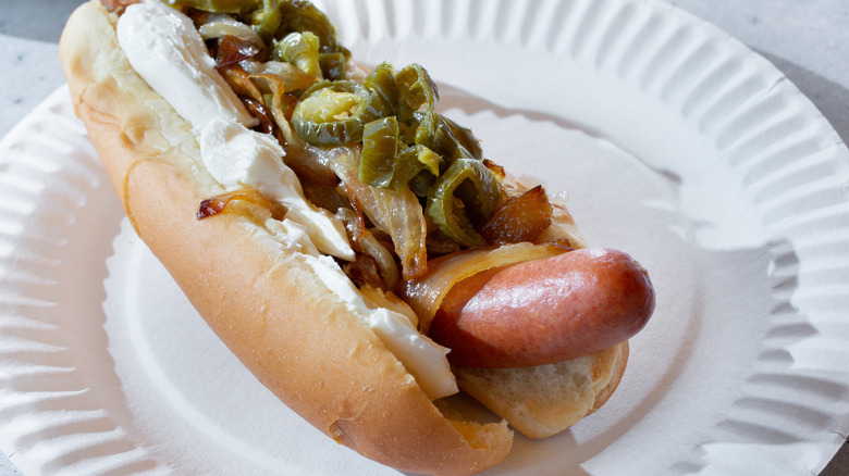 Seattle hot dog on a white plate, topped with cream cheese, grilled onions and jalapenos