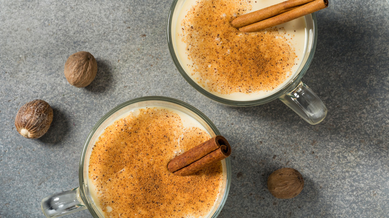 Two glass mugs of eggnog with cinnamon sticks in them