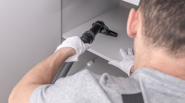 Person wearing gloves vacuuming an empty pantry shelf