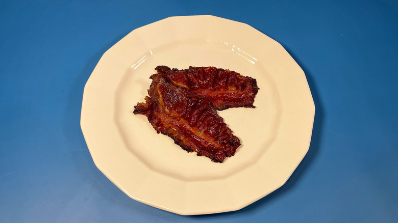 Two pieces of cooked Certified Angus Beef bacon on a white plate and blue background
