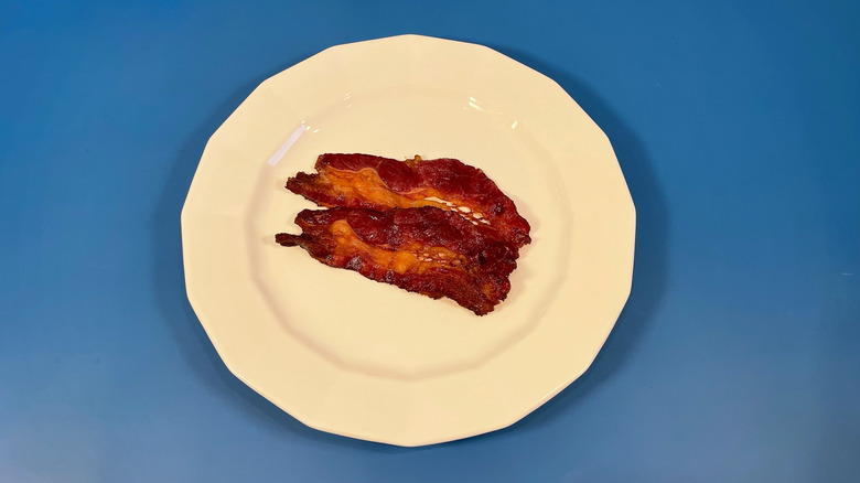 Two pieces of cooked Godshall's bacon on a white plate and blue background